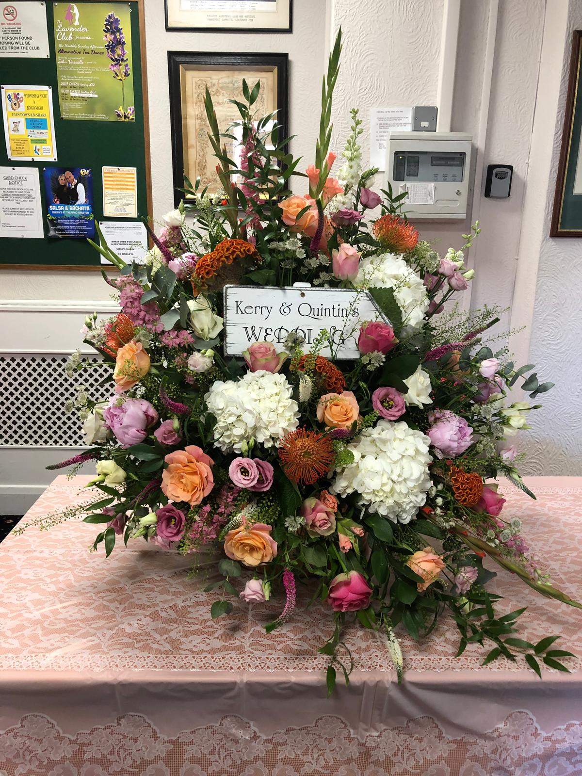 Large floral display with a Kerry and Quintin's wedding sign at a catered reception