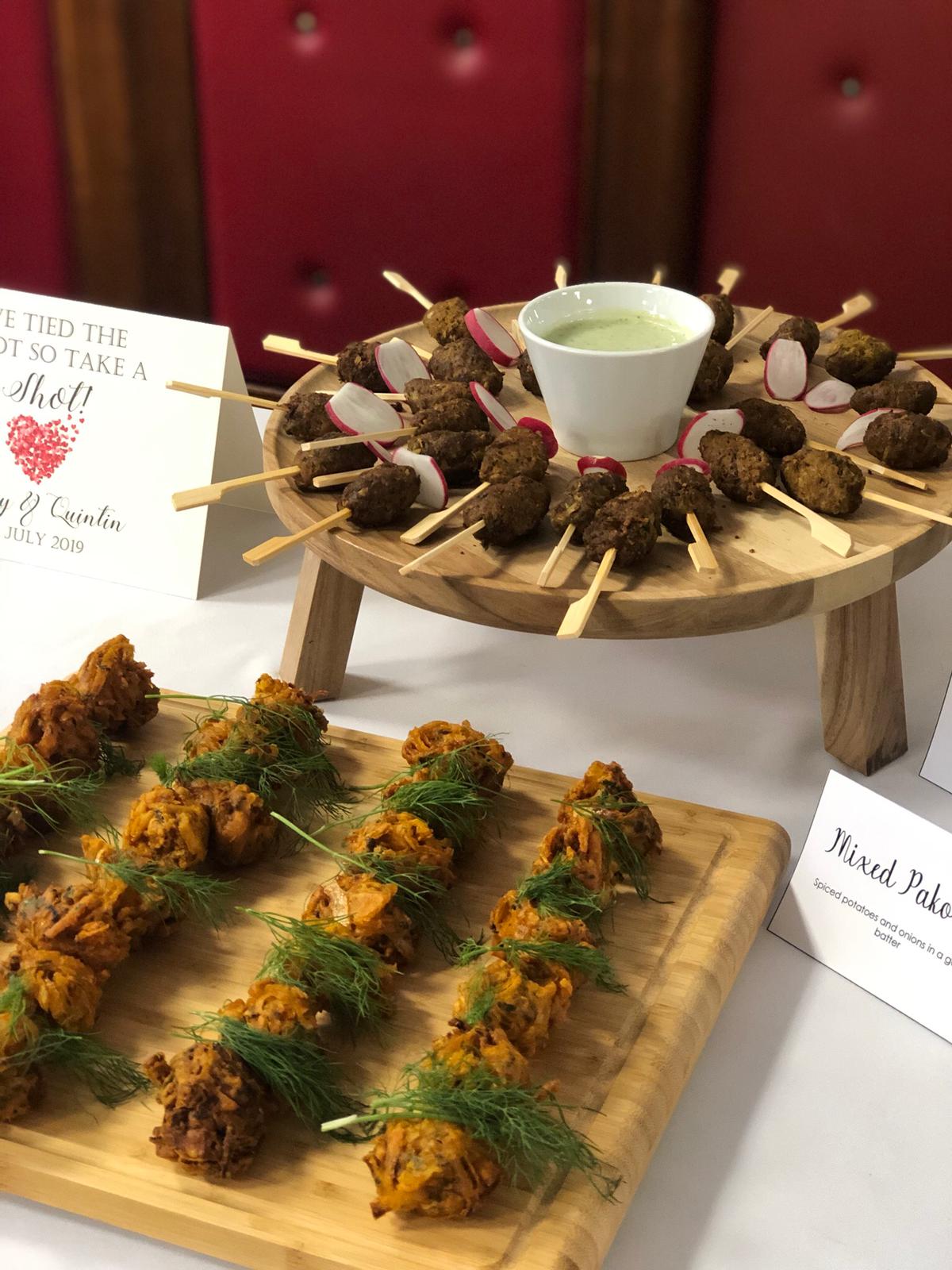 Seekh kebab skewers and mixed pakoras plated on wooden boards with mint dip