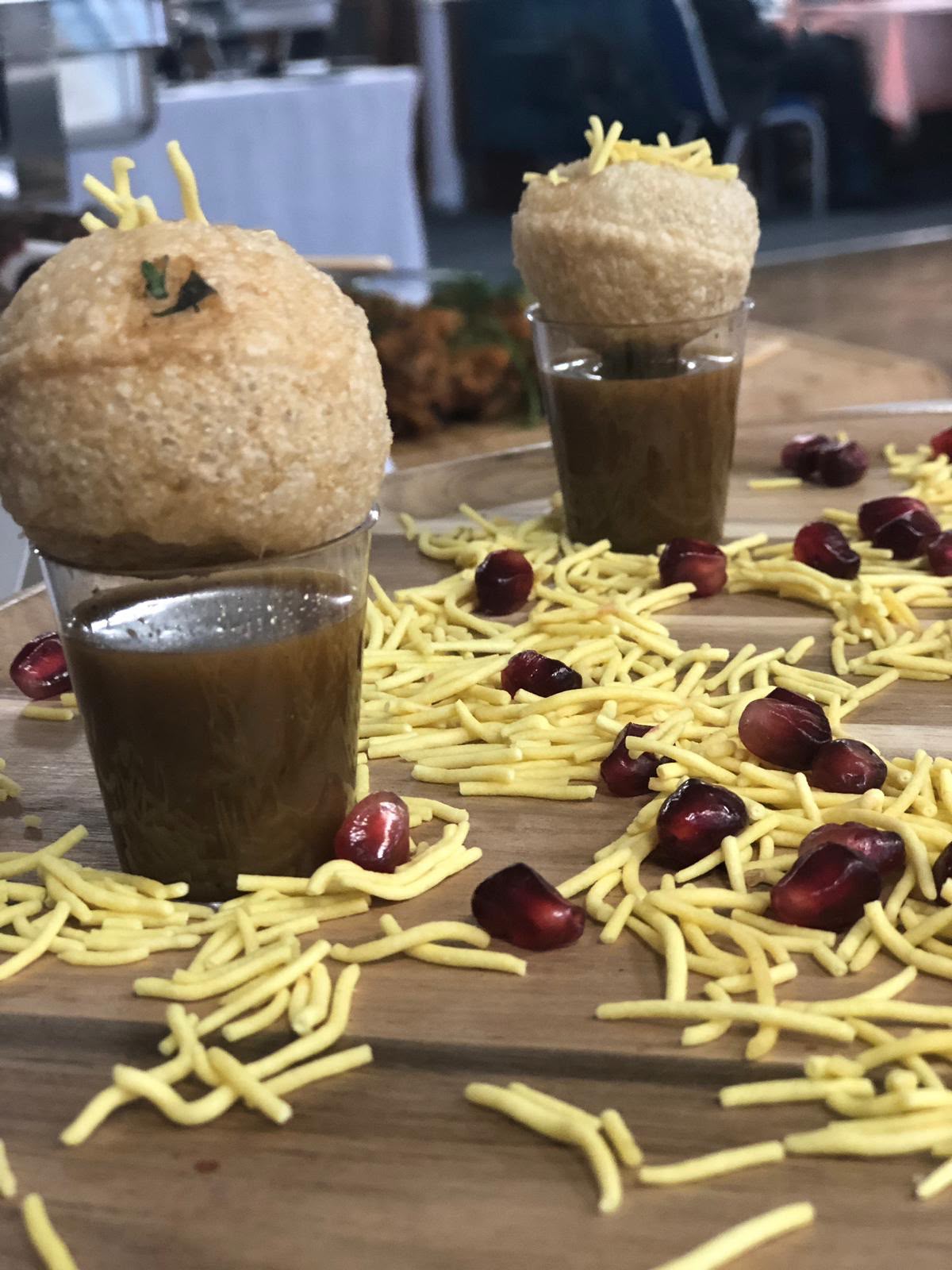 Close-up of pani puri shot glasses topped with pomegranate seeds and fresh coriander