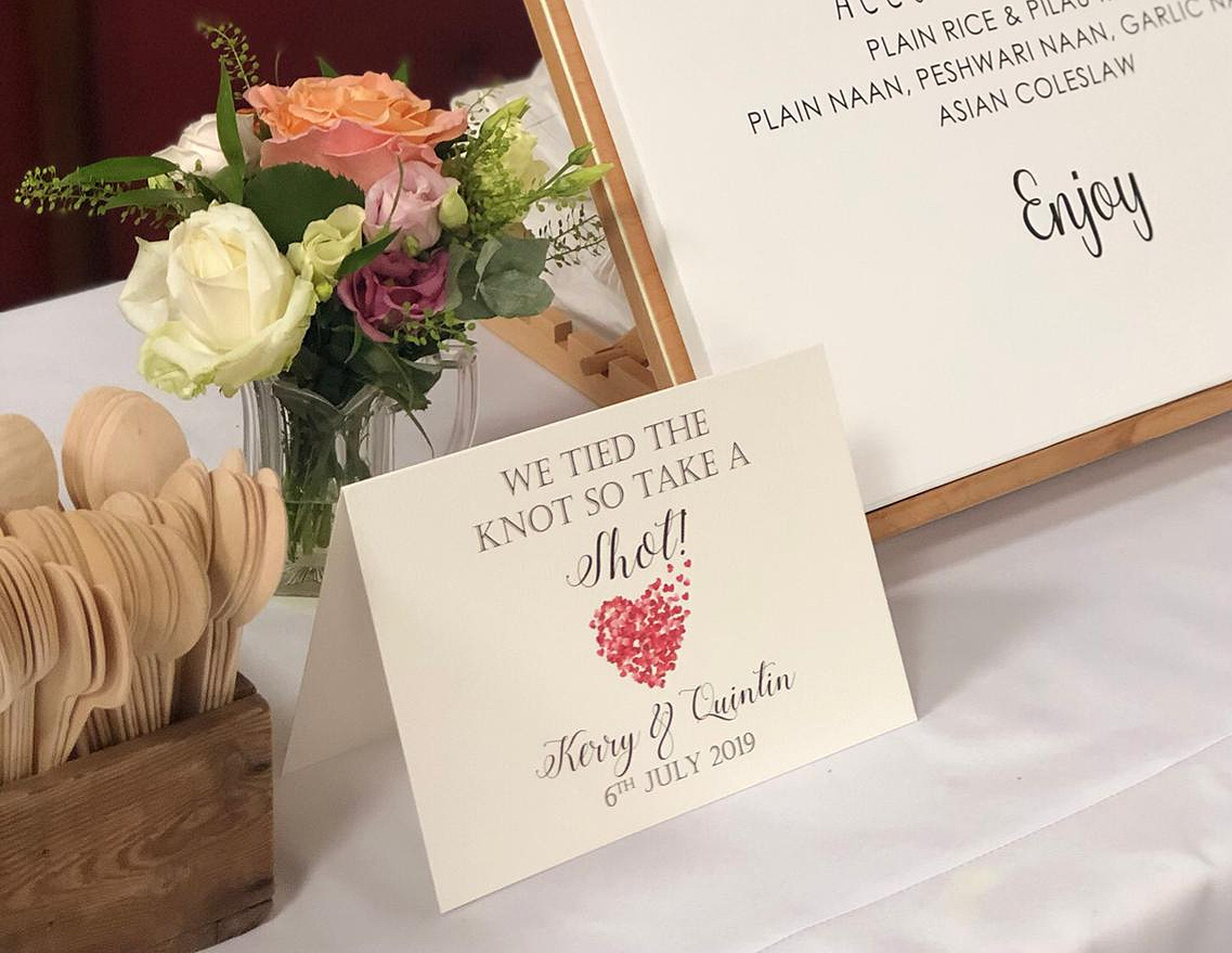 Wedding menu signage and fresh flowers on a linen-covered catering table